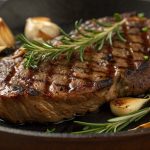 Juicy rib eye steak cooked in the oven, resting on a pan with herbs and garlic for a flavorful, tender finish.