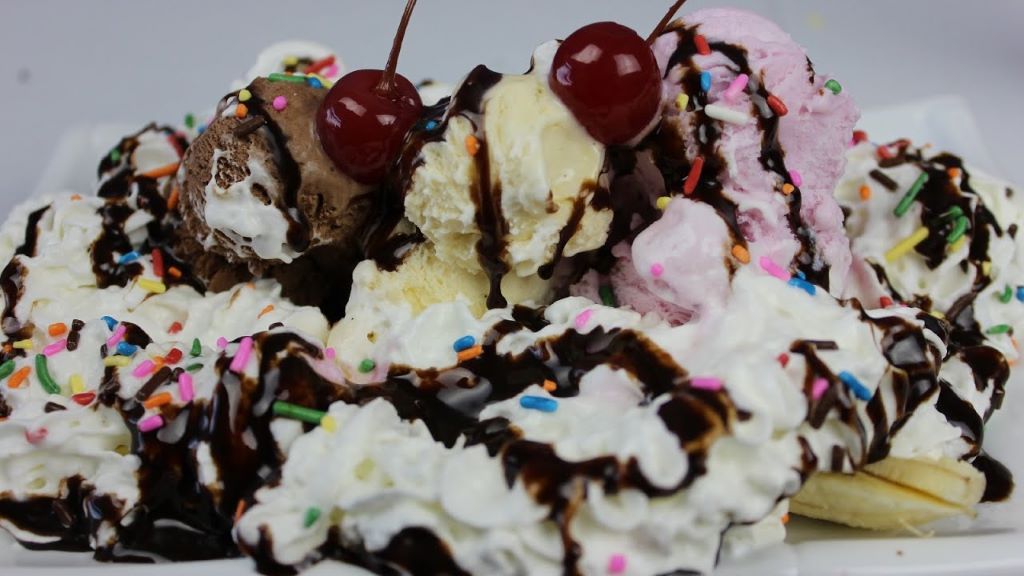 Kids decorating a banana split pie with chocolate syrup and nuts