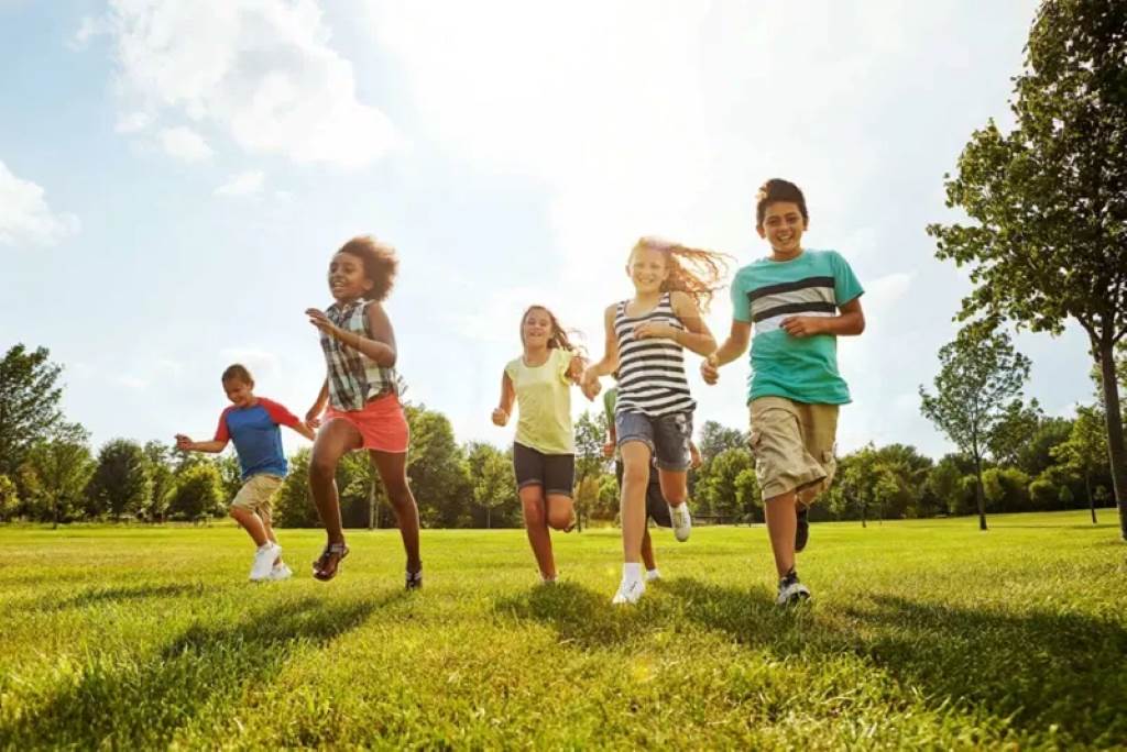 Kids play on a grassy field with parents supervising, enjoying outdoor activities at a preschool co-op
