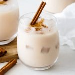 A glass of creamy horchata with a cinnamon stick garnish on a wooden table