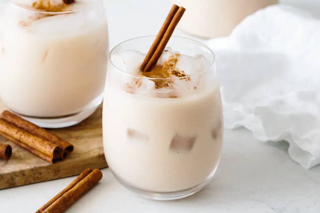 A glass of creamy horchata with a cinnamon stick garnish on a wooden table